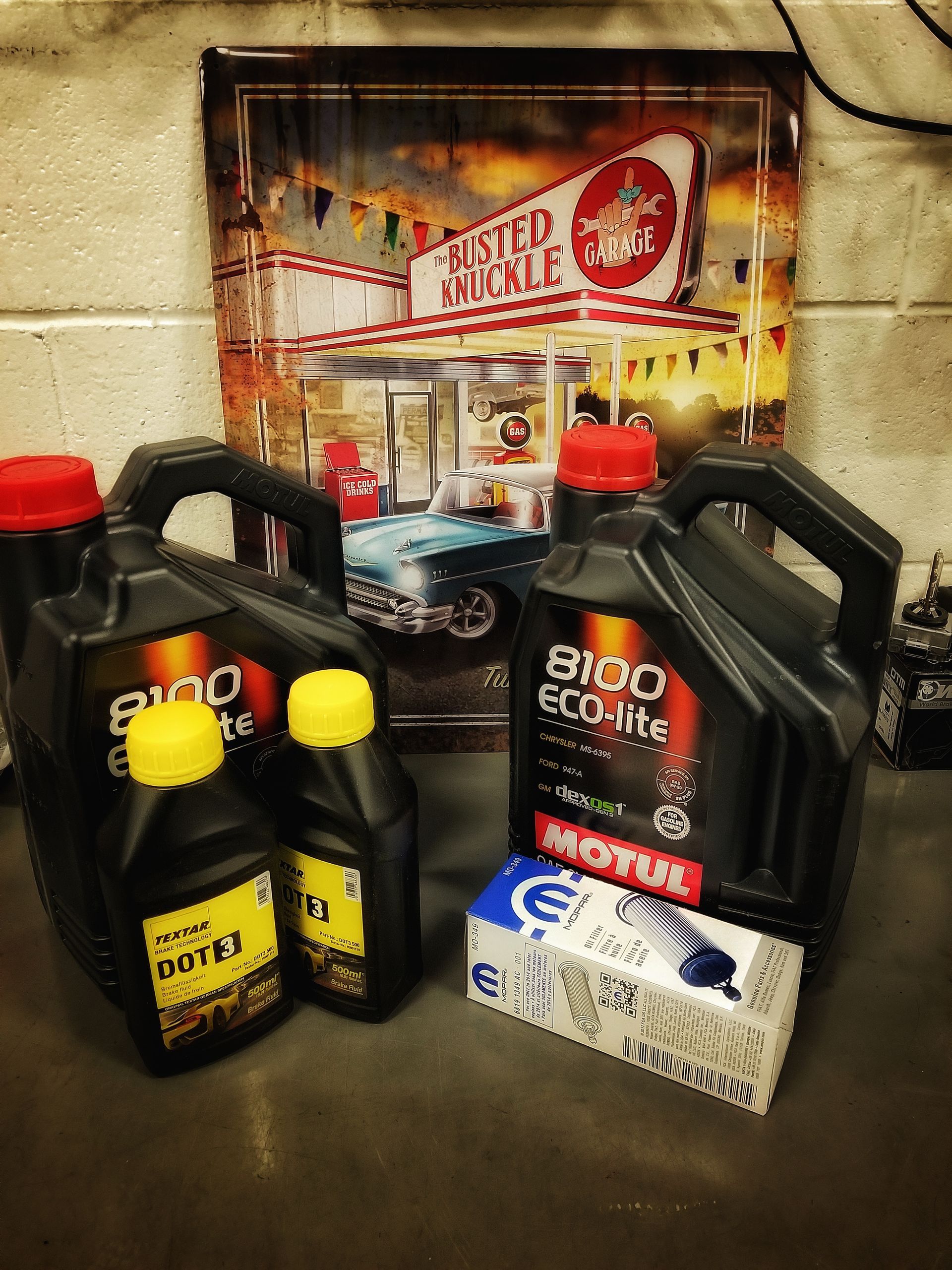 Black oil containers, a box, and a poster with a diner scene are on a counter. | Mecano Autoworks