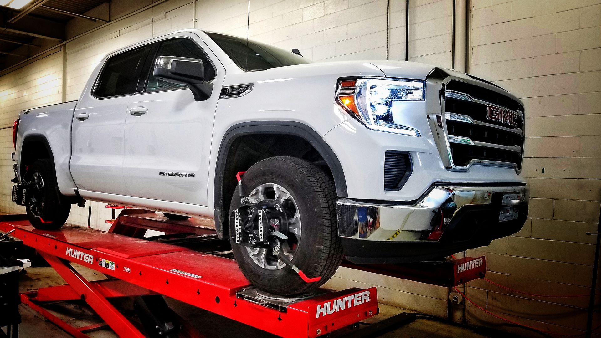 White GMC truck on a red Hunter alignment lift inside a garage. | Mecano Autoworks