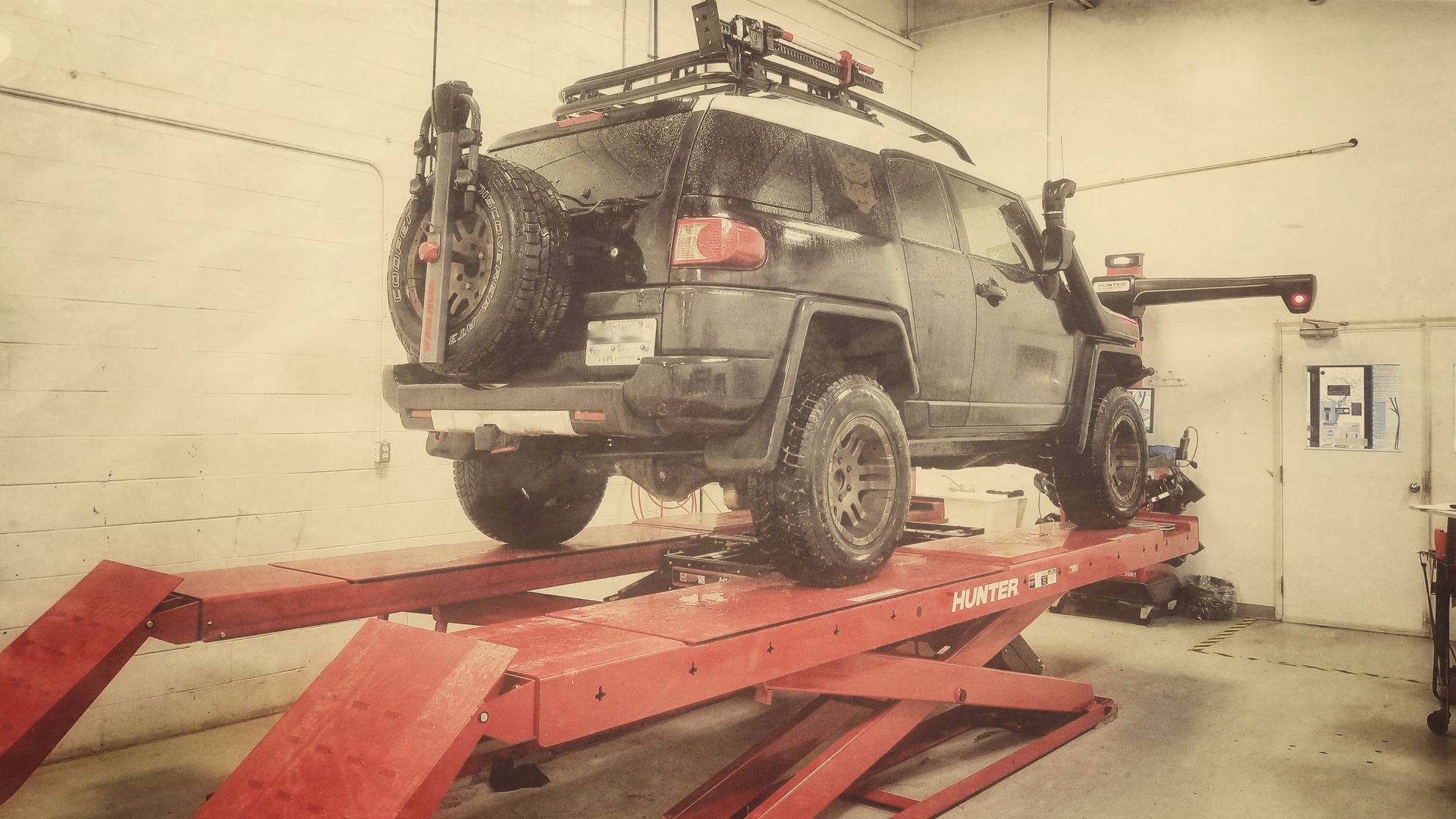 Black FJ Cruiser SUV on a red car lift inside a garage. | Mecano Autoworks