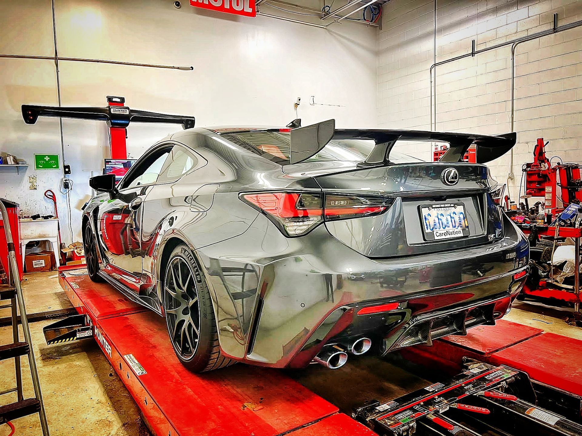 Gray Lexus RC F coupe on a red lift in a garage, with a large rear wing, preparing for maintenance. | Mecano Autoworks
