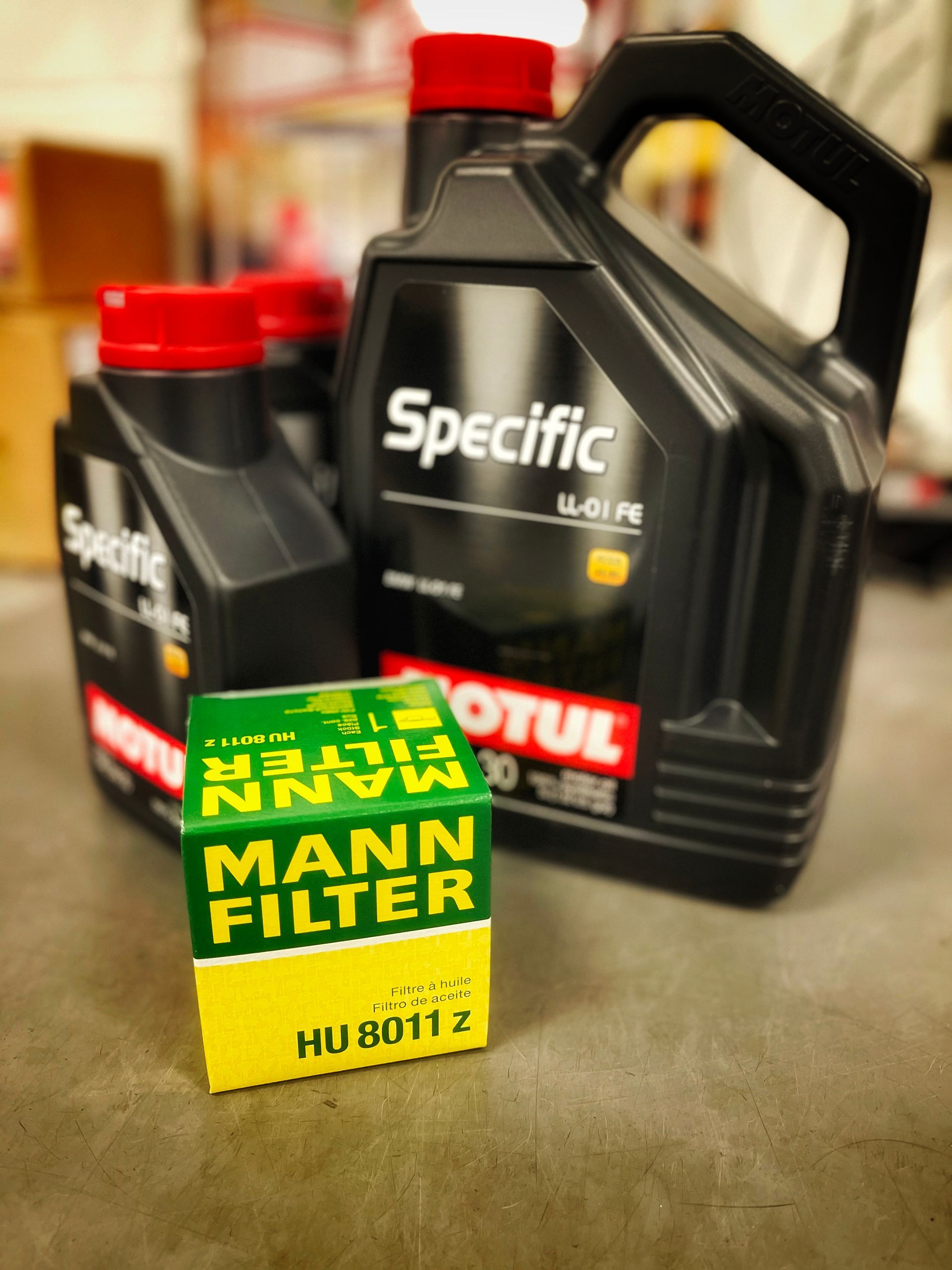 Oil bottles and oil filter box on a garage floor. Black oil bottles, and a green and yellow filter box. | Mecano Autoworks