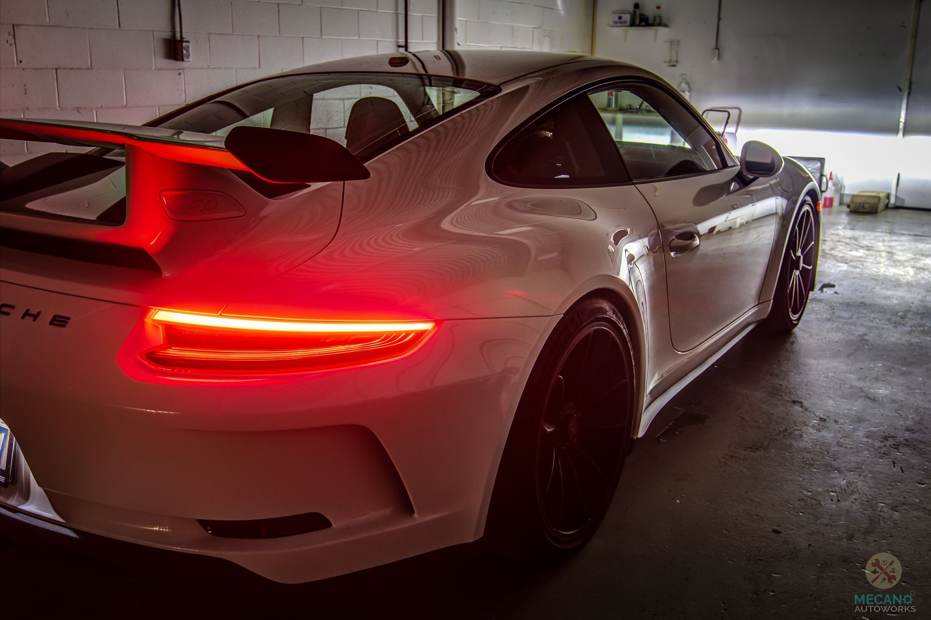 White Porsche sports car with red taillights, parked indoors. | Mecano Autoworks