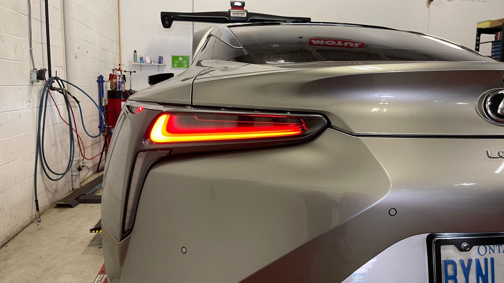 Silver Lexus car with illuminated red tail lights, parked inside a garage. | Mecano Autoworks