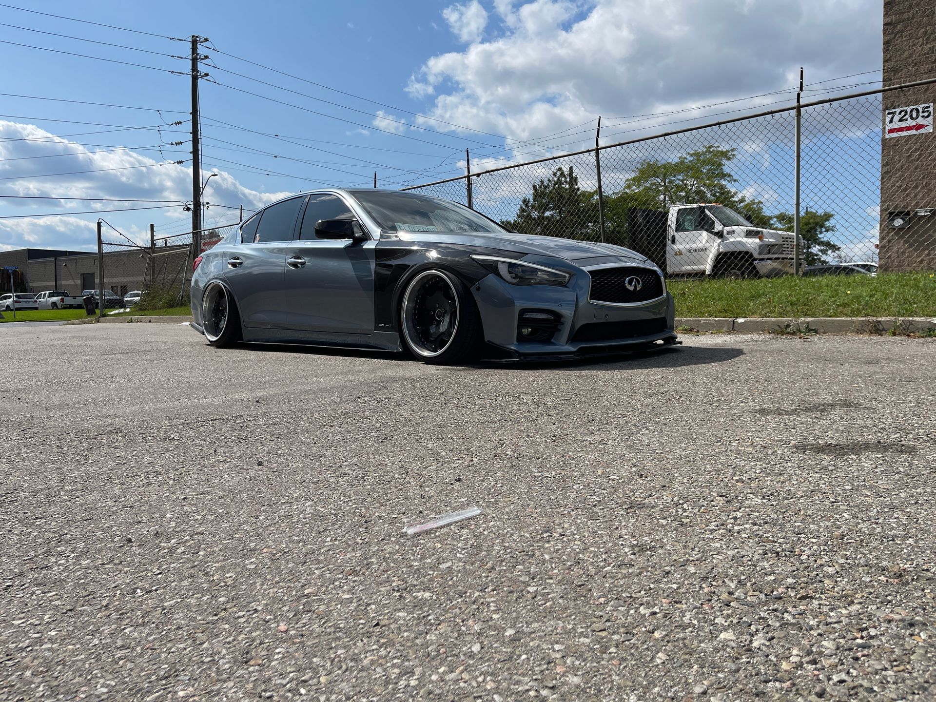 Slammed grey Infiniti sedan with black wheels, parked on a cracked asphalt lot under a sunny sky. | Mecano Autoworks