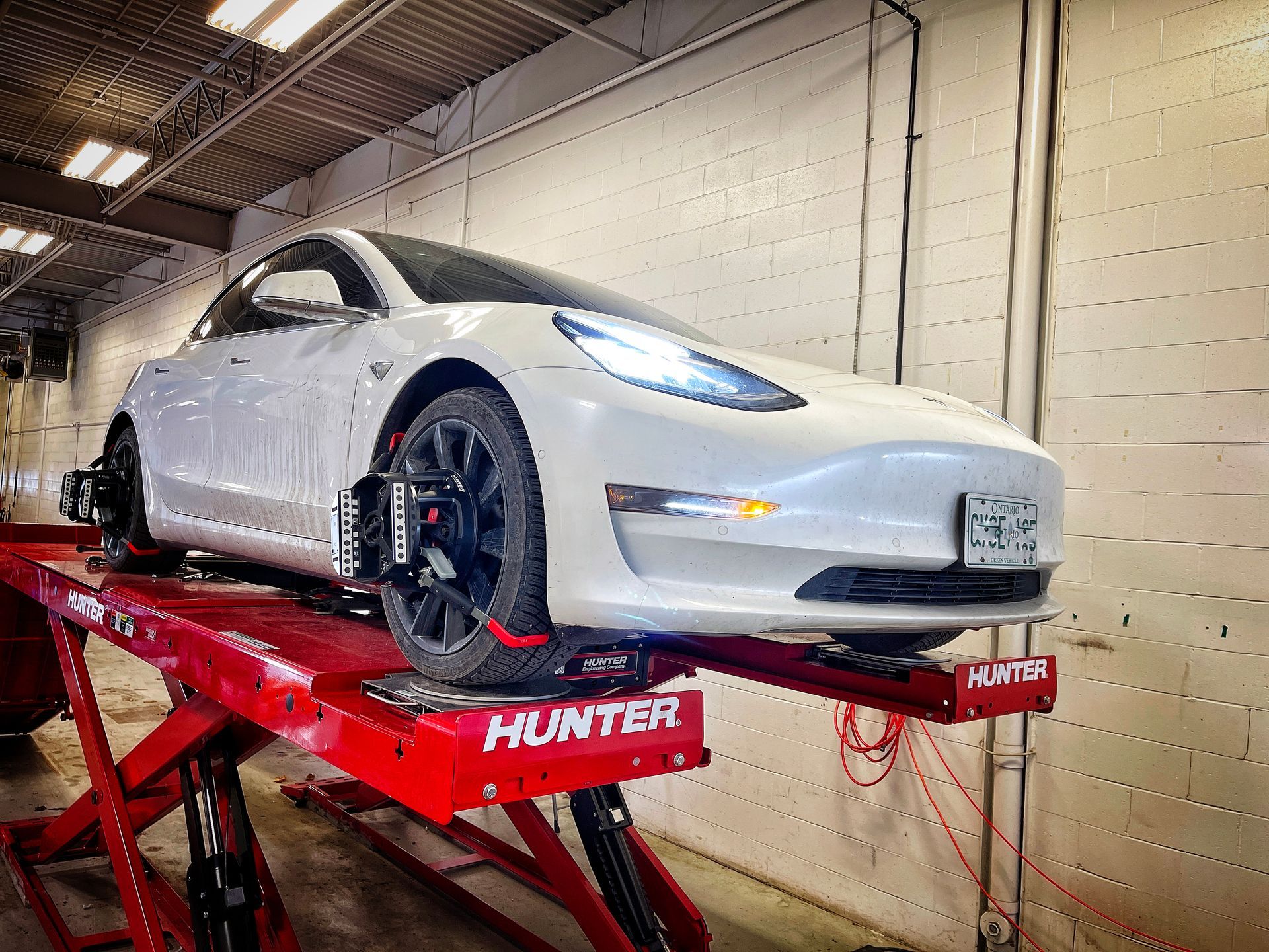 White Tesla on a red Hunter alignment lift in a garage, being serviced. | Mecano Autoworks