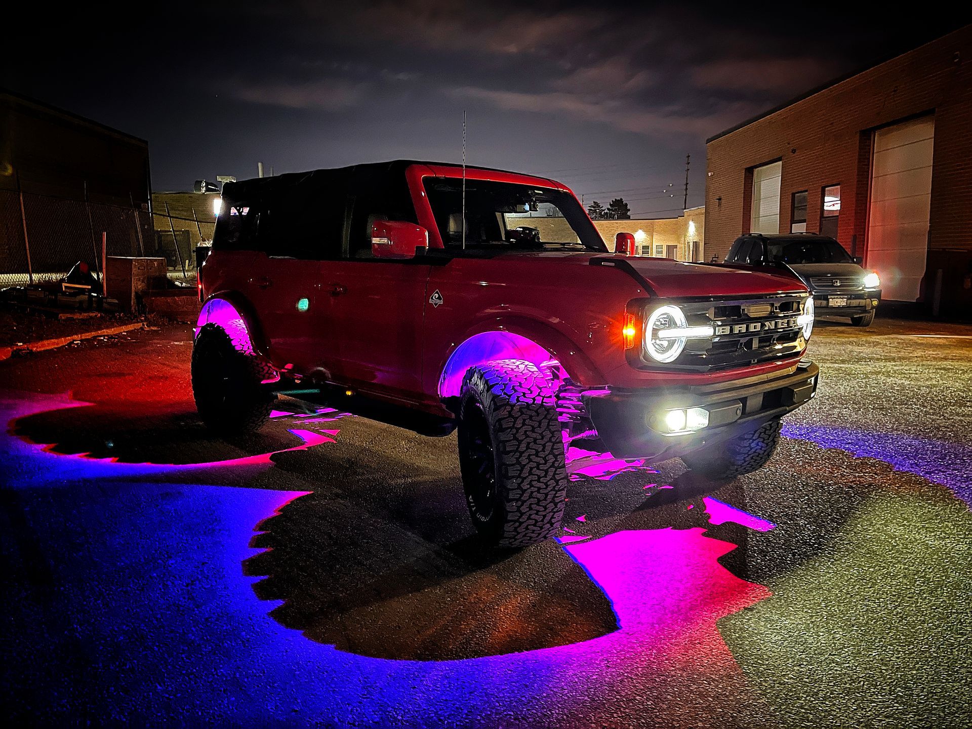 Red Ford Bronco SUV with colorful underglow lighting parked at night. | Mecano Autoworks