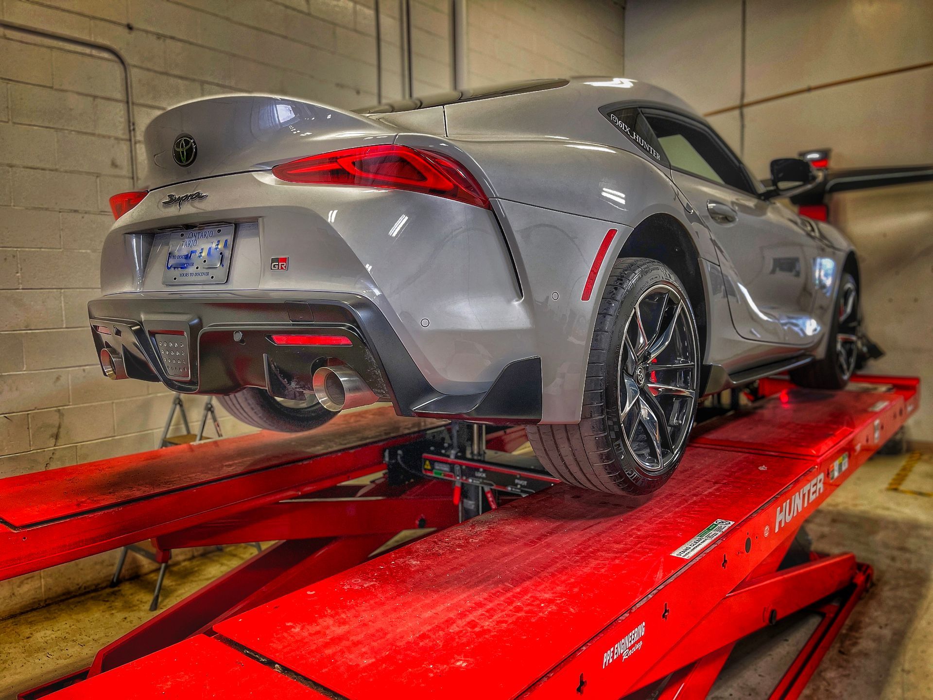 Gray Toyota Supra sports car on a red car lift in a garage. | Mecano Autoworks