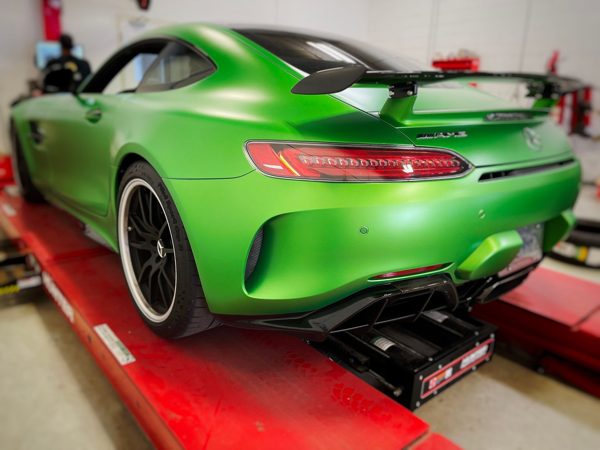 Green Mercedes-AMG GT on a lift; black spoiler, white wheels, in a garage. | Mecano Autoworks