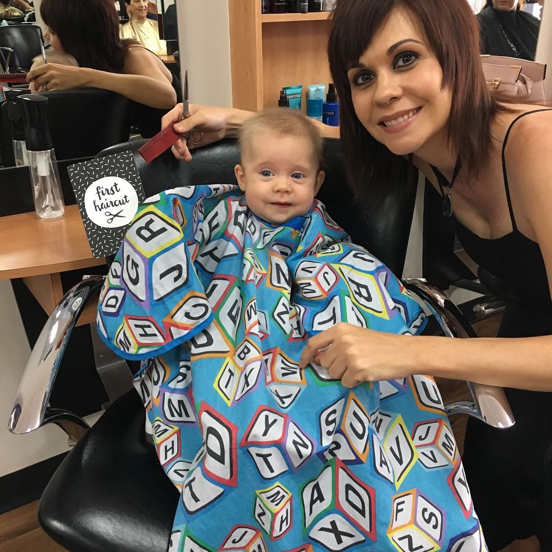 Woman and baby at a salon; baby in cape, woman holding comb, smiling — EDISON Hair Collective In Mackay, QLD