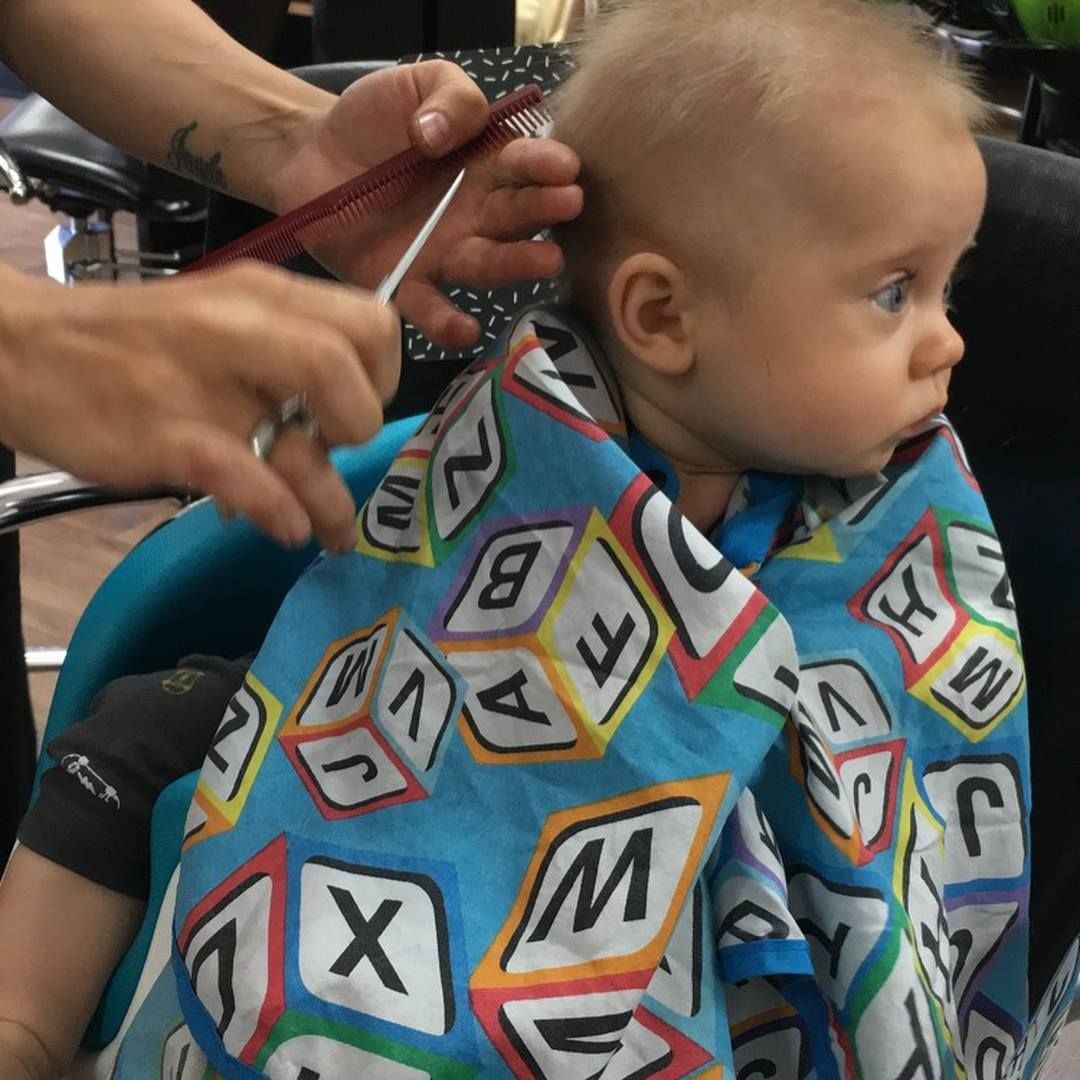Baby Getting a Haircut, Wearing a Blue Cape with Alphabet Blocks, Looking Away from The Scissors — EDISON Hair Collective In Mackay, QLD