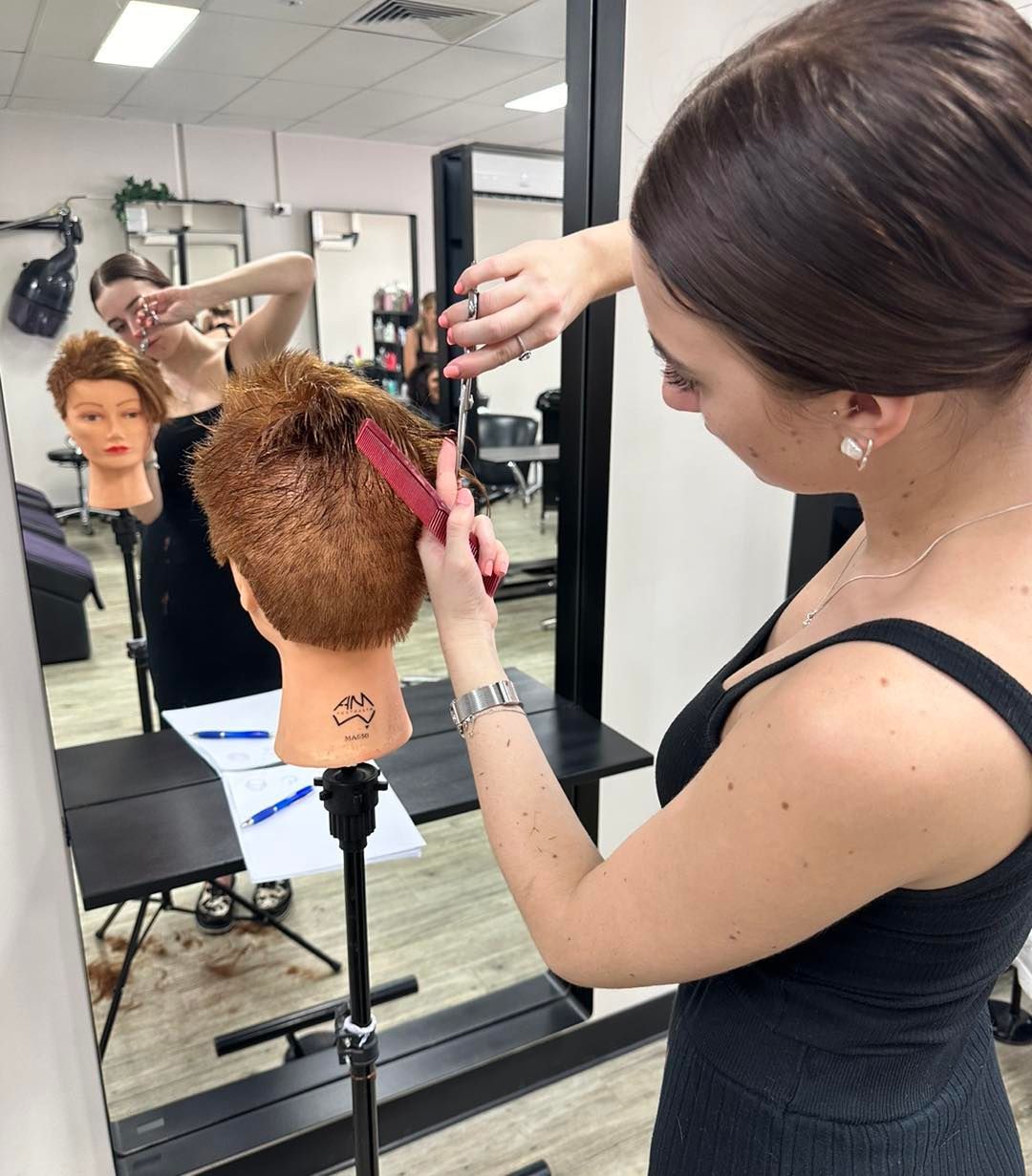 Woman Cutting Hair on a Mannequin. She Holds a Comb and Scissors, in a Salon — EDISON Hair Collective In Mackay, QLD