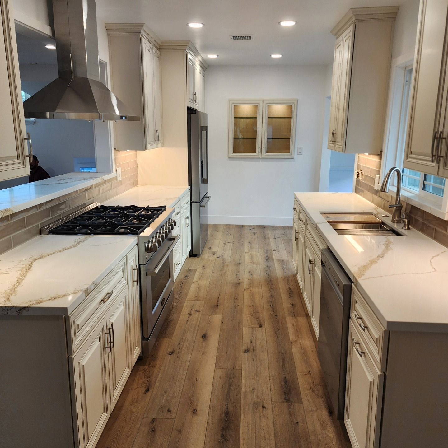 Long, narrow kitchen with white cabinets, stainless steel appliances, and wood flooring. Chino / 91710