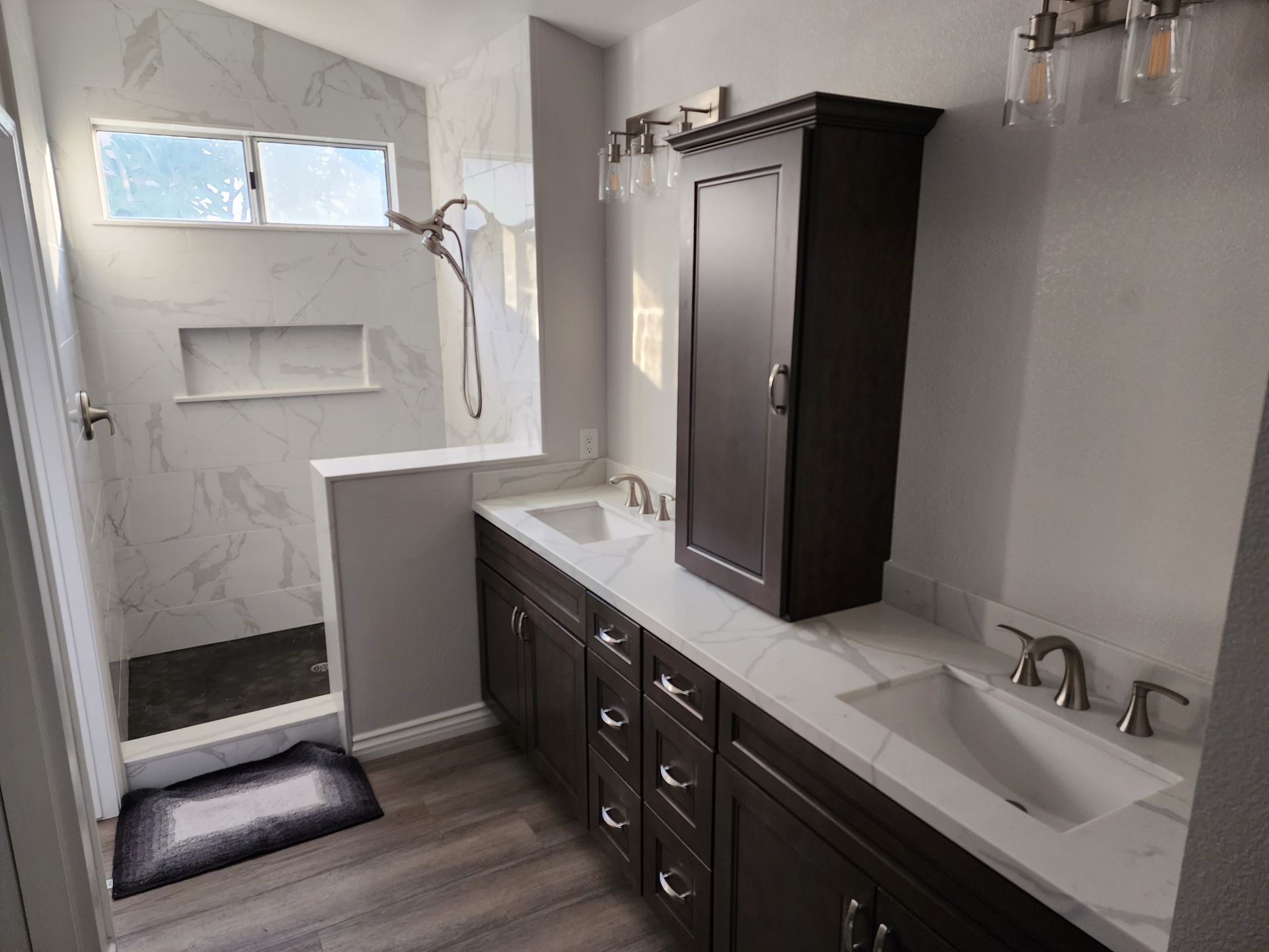 Bathroom with dark brown cabinetry, white countertops, and a walk-in shower with marble tile.