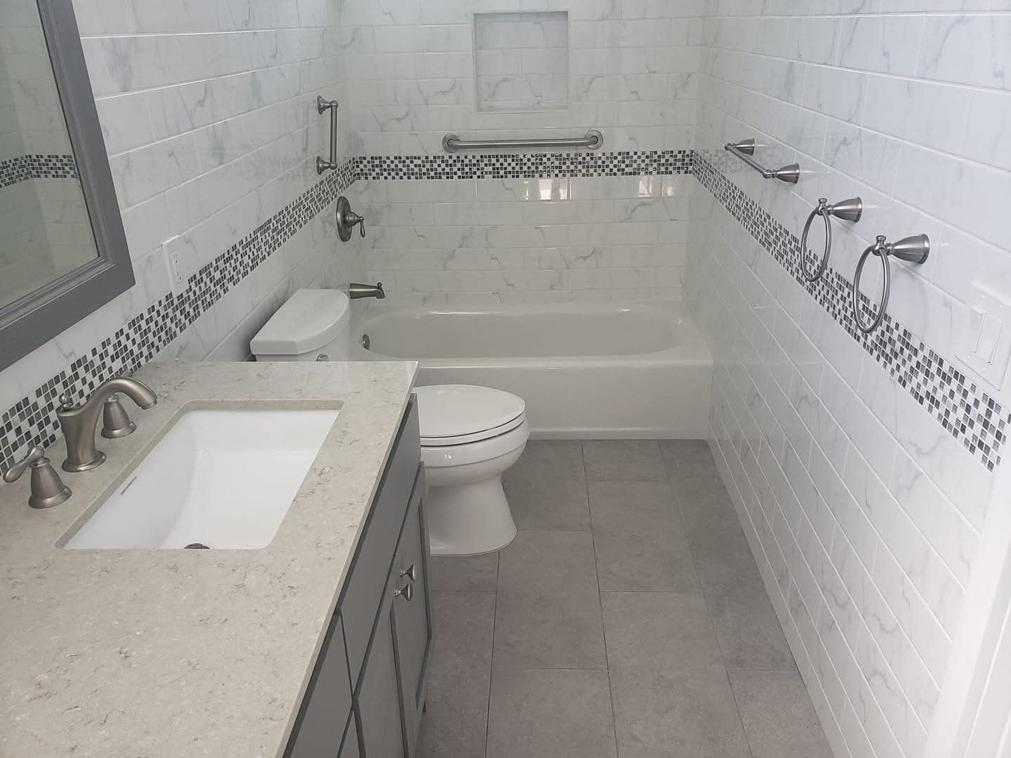 Bathroom with white subway tiles, a mosaic border, a bathtub, and a vanity.