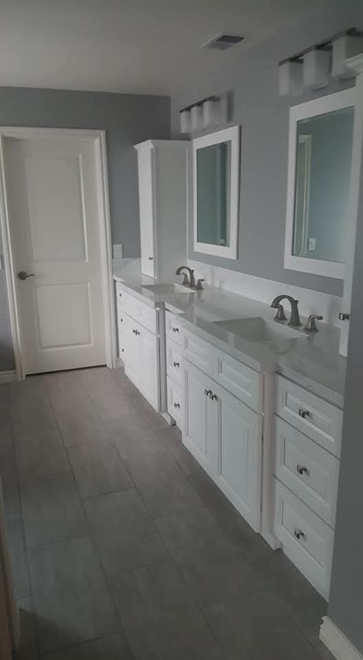 Bathroom with white cabinets, gray walls, two mirrors with sconces, and a white door. Chino/91710