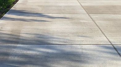 A close up of a concrete driveway with shadows of trees on it.