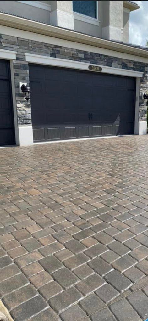 A brick driveway with a black garage door in front of a house.