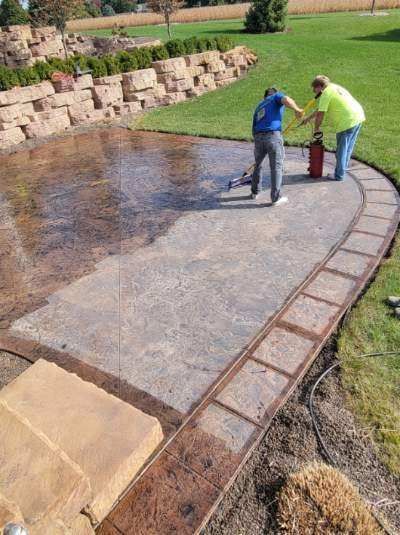 Two men are painting a concrete walkway in a backyard.