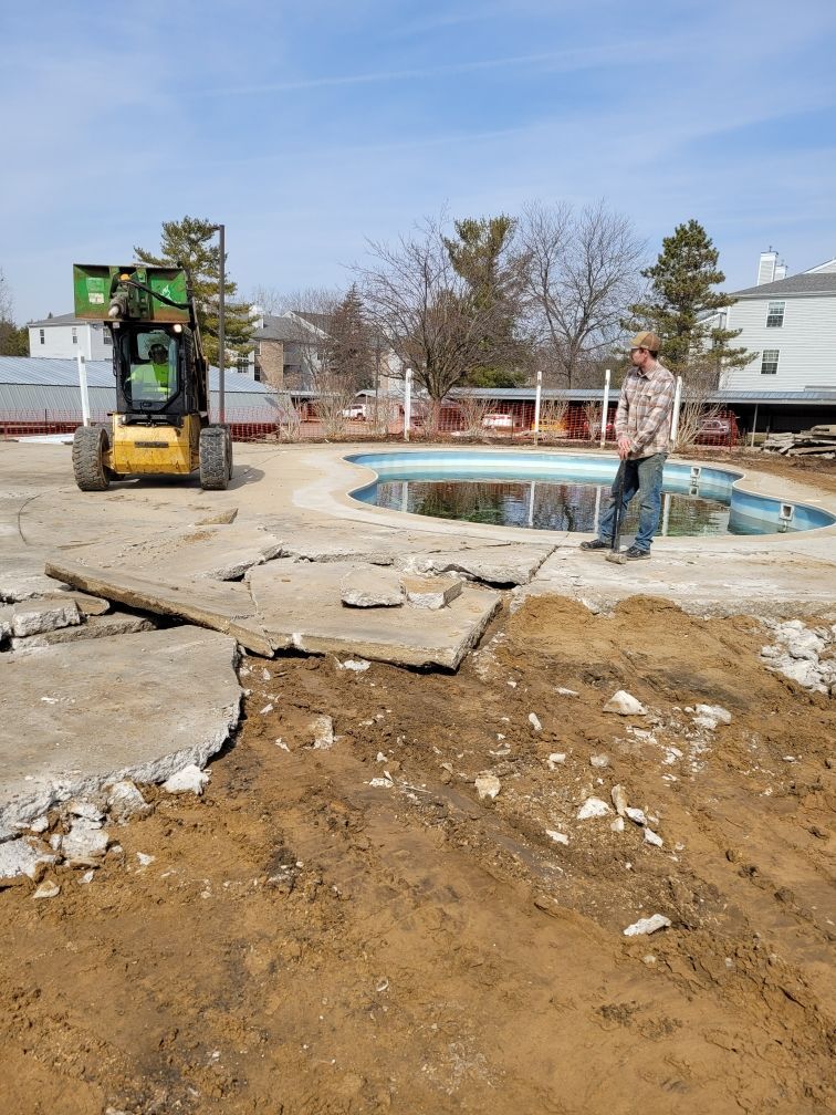 A man is standing in a dirt field next to a swimming pool.