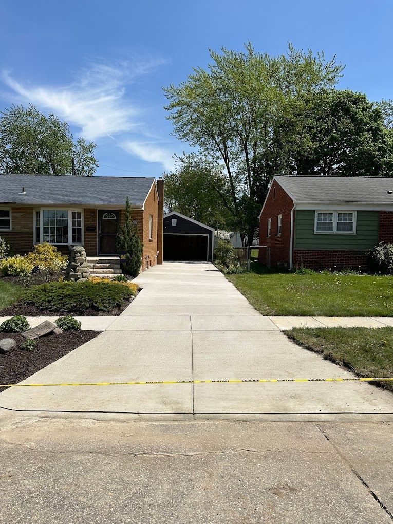 A concrete driveway leading to a brick house and a green house.