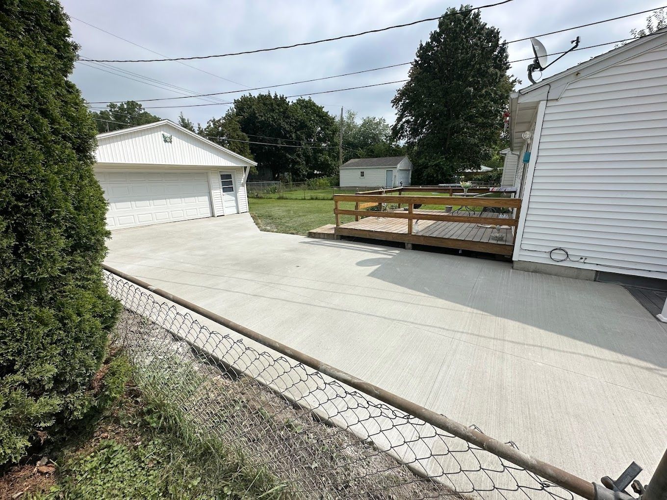 A concrete driveway leading to a white house with a wooden deck.