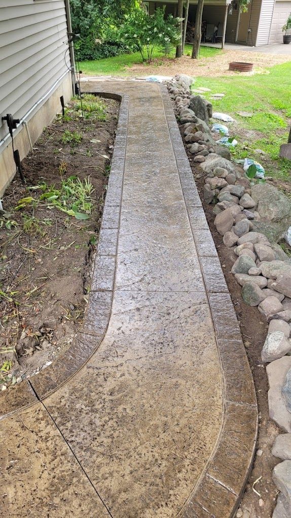 A concrete walkway leading to a house next to a rock wall.