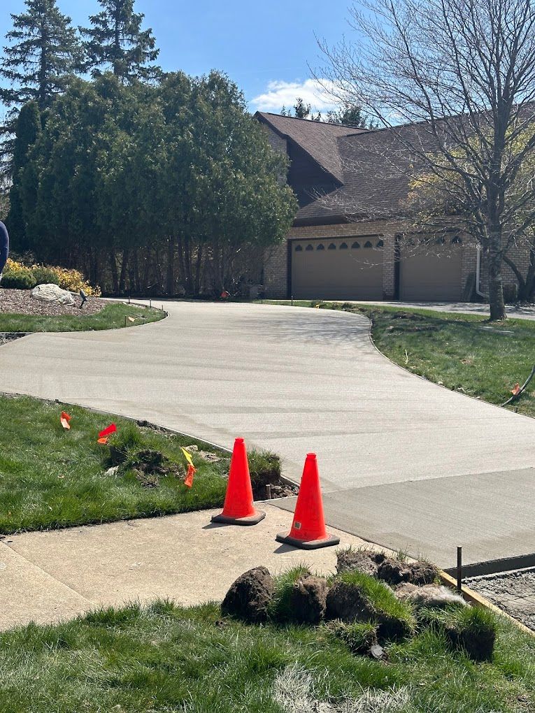 Two orange traffic cones are sitting on a concrete driveway in front of a house.