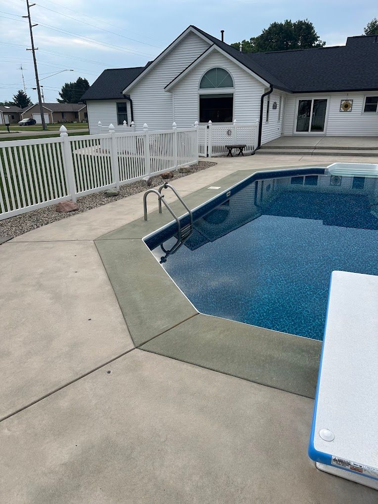 A swimming pool in front of a house with a white fence