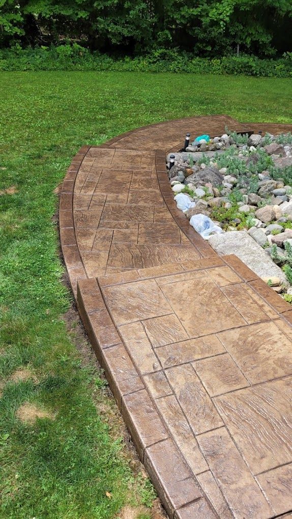 A concrete walkway is surrounded by grass and rocks in a backyard.