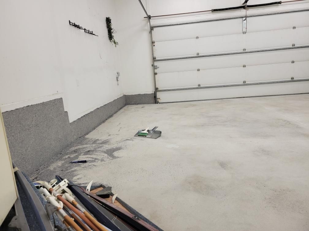 A garage with a garage door open and a bunch of tools on the floor.