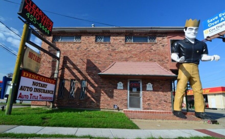 Building with giant statue of a man wearing a crown, offering notary, auto insurance, and title services.