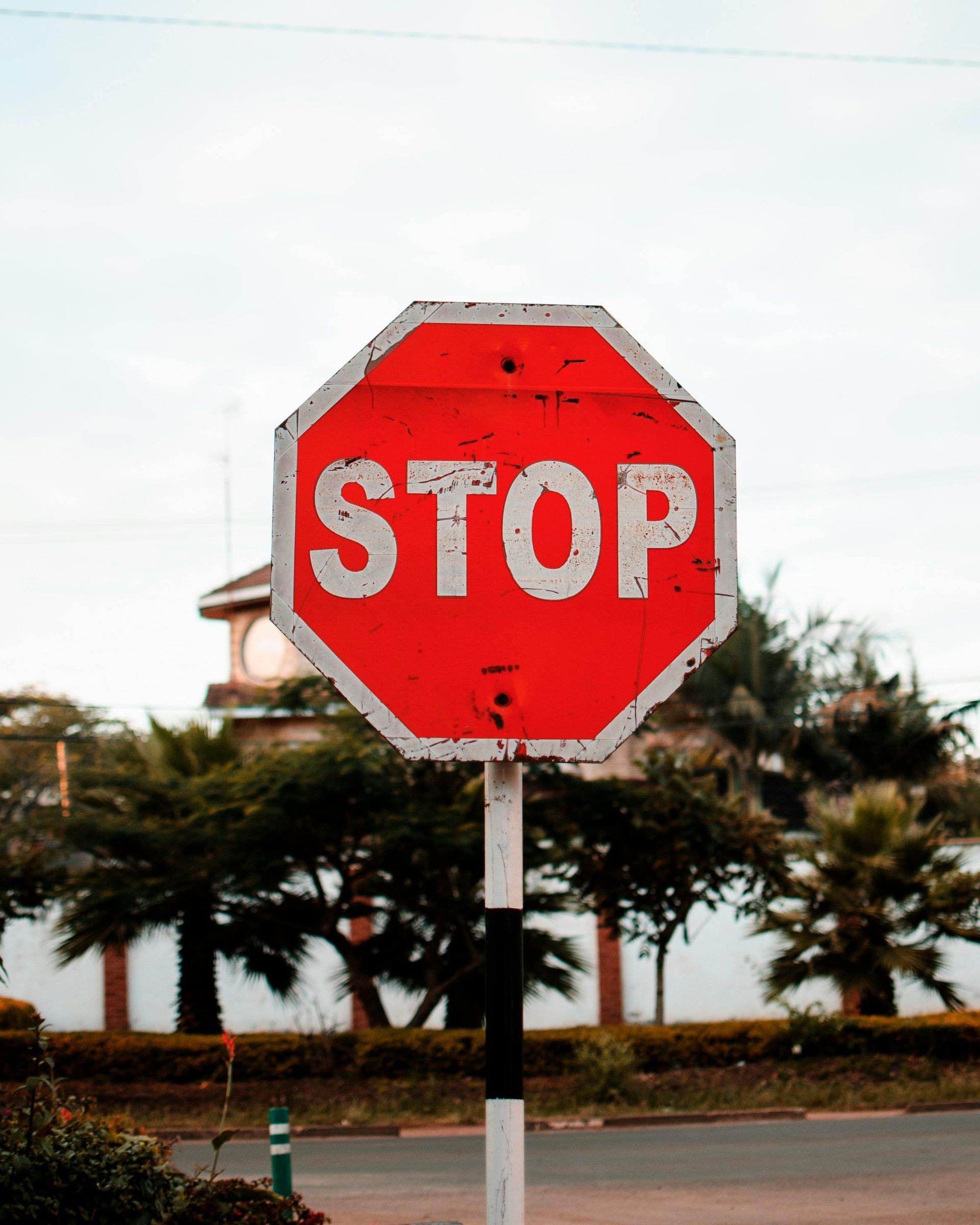 Red stop sign with white text, on a black and white striped post, outdoors.