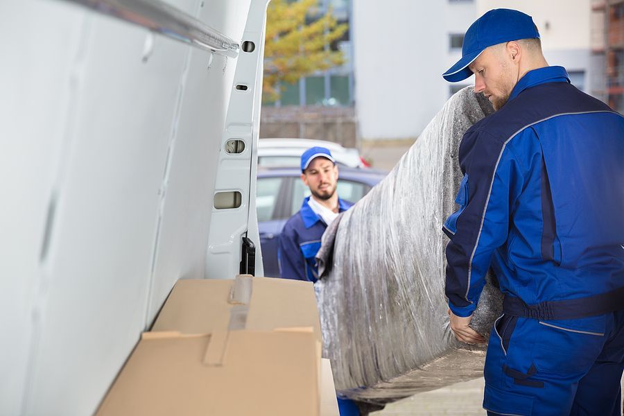 Moving crew loading a wrapped mattress into the back of a van.