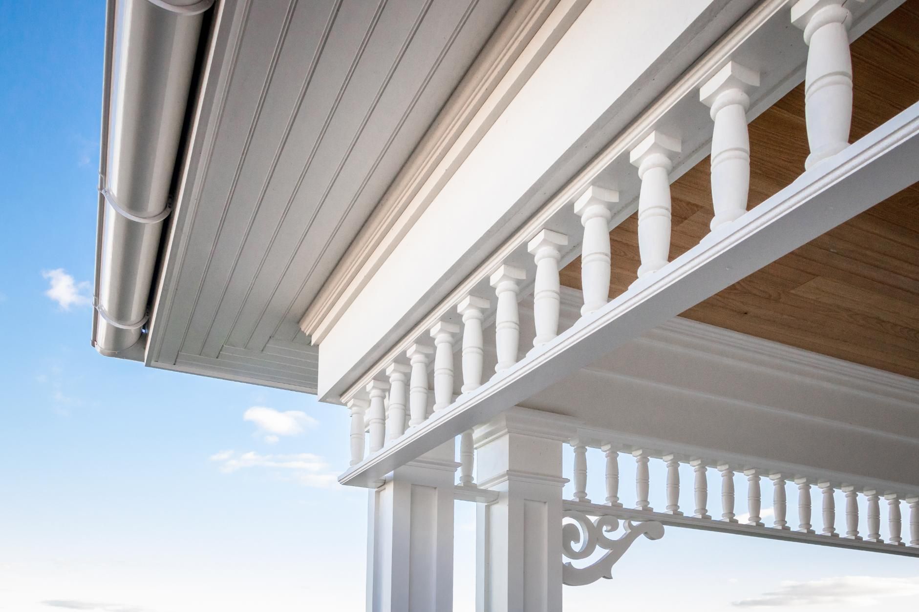 White porch with balustrade and decorative brackets against a blue sky.