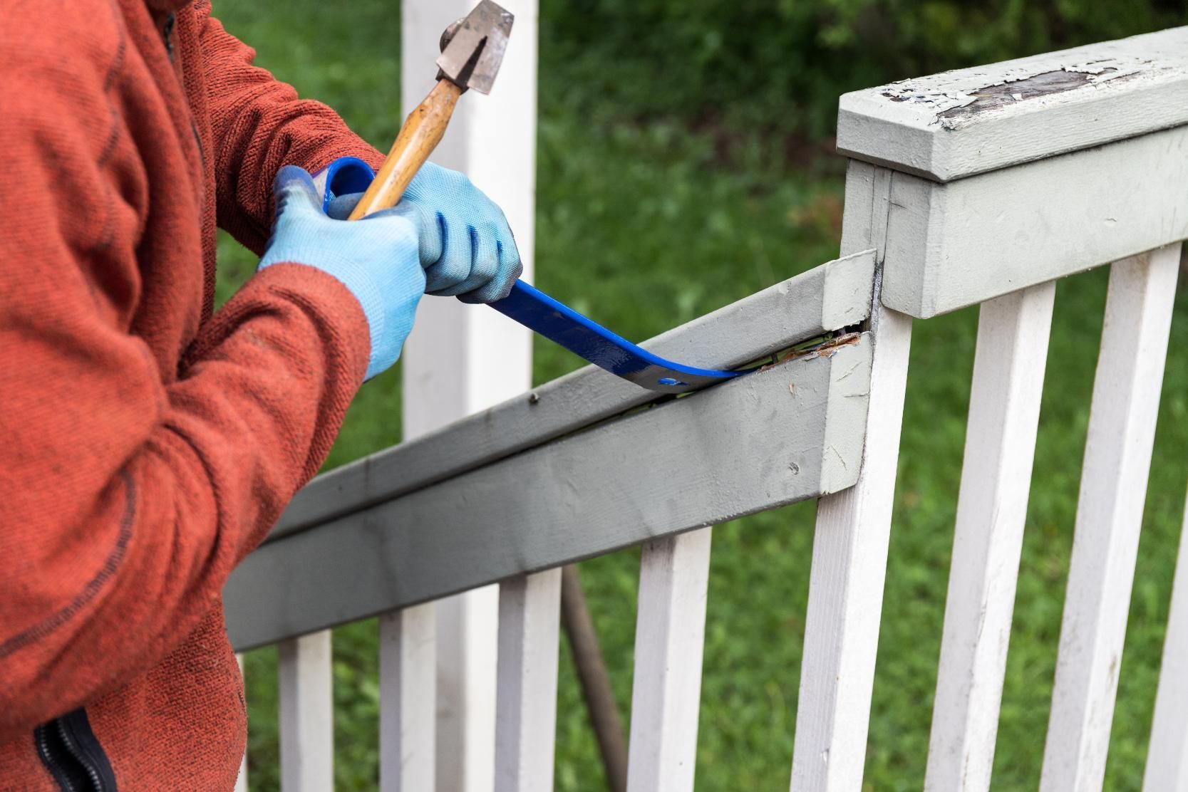 Person using a crowbar and hammer to remove a section of a painted white railing.