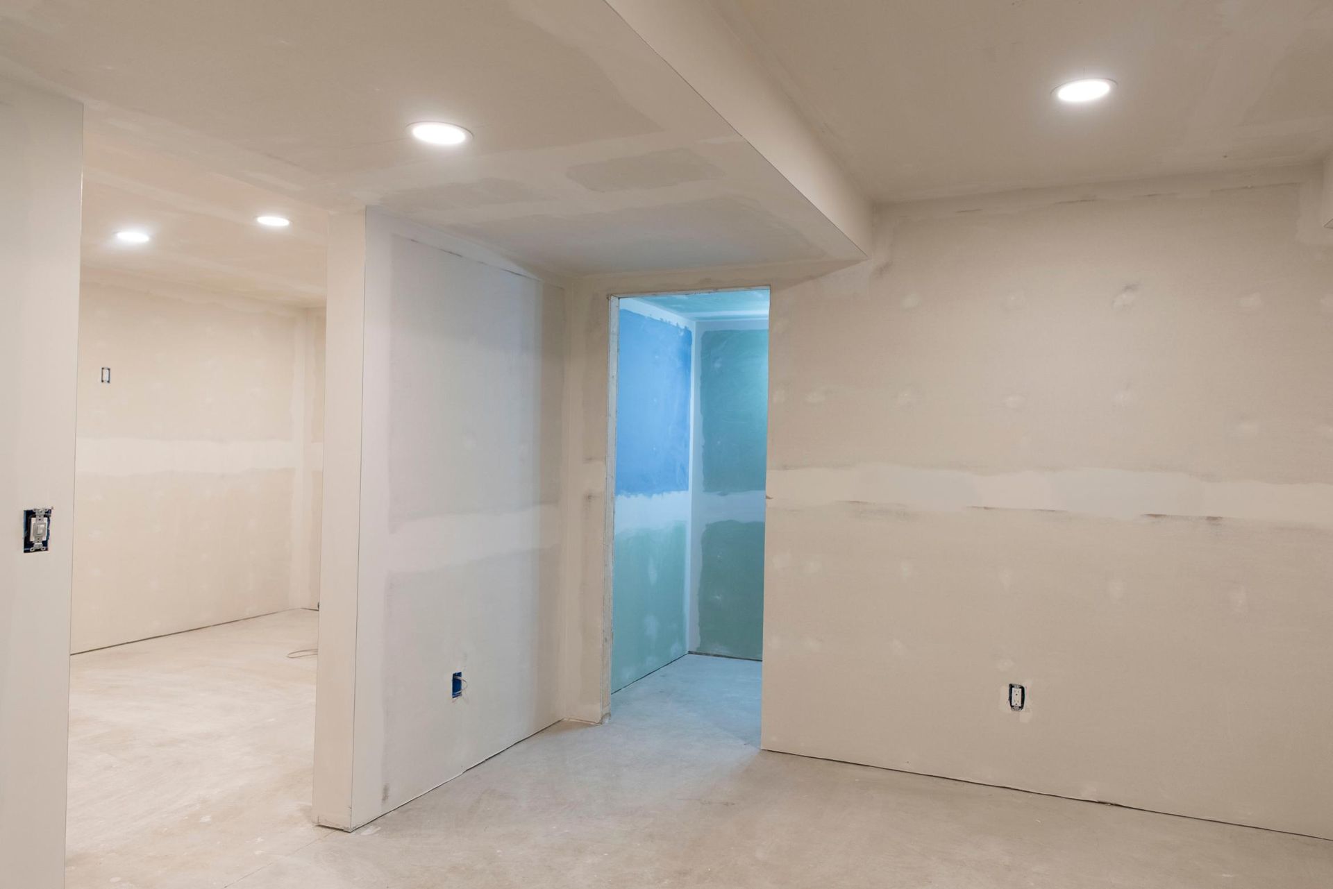 Interior of a room under construction with drywall and recessed lighting.