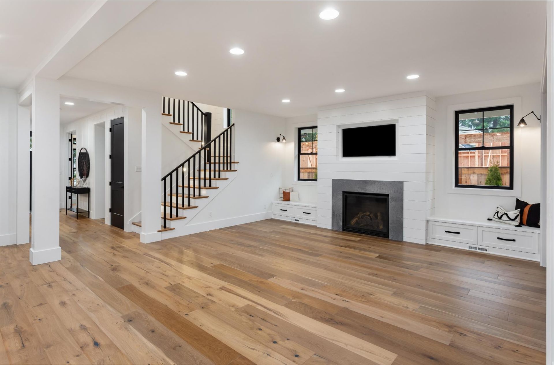 Spacious, light-filled living room with hardwood floors, a fireplace, and a staircase.