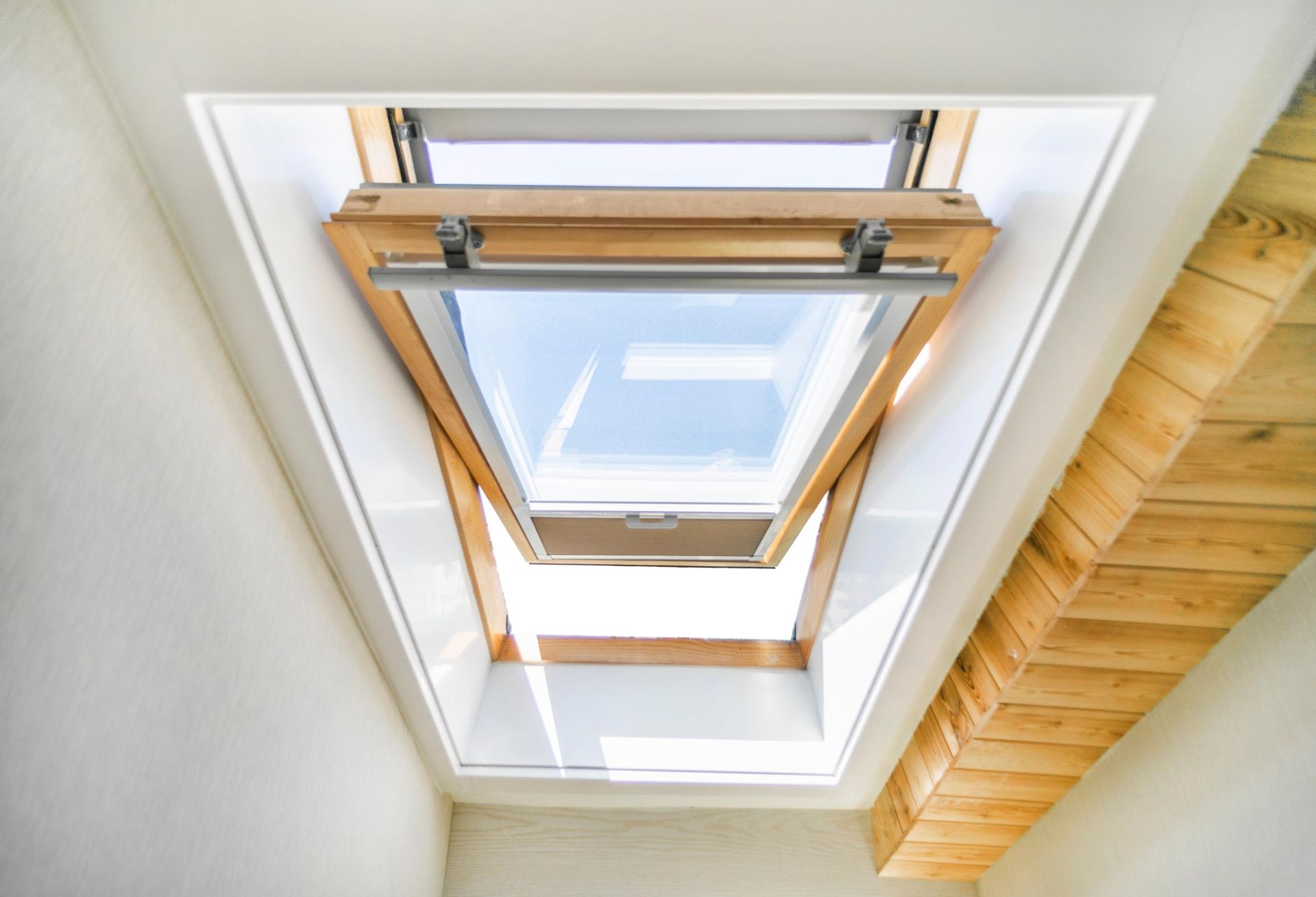 Open skylight in a white-walled room with wooden framing and a view to the sky.