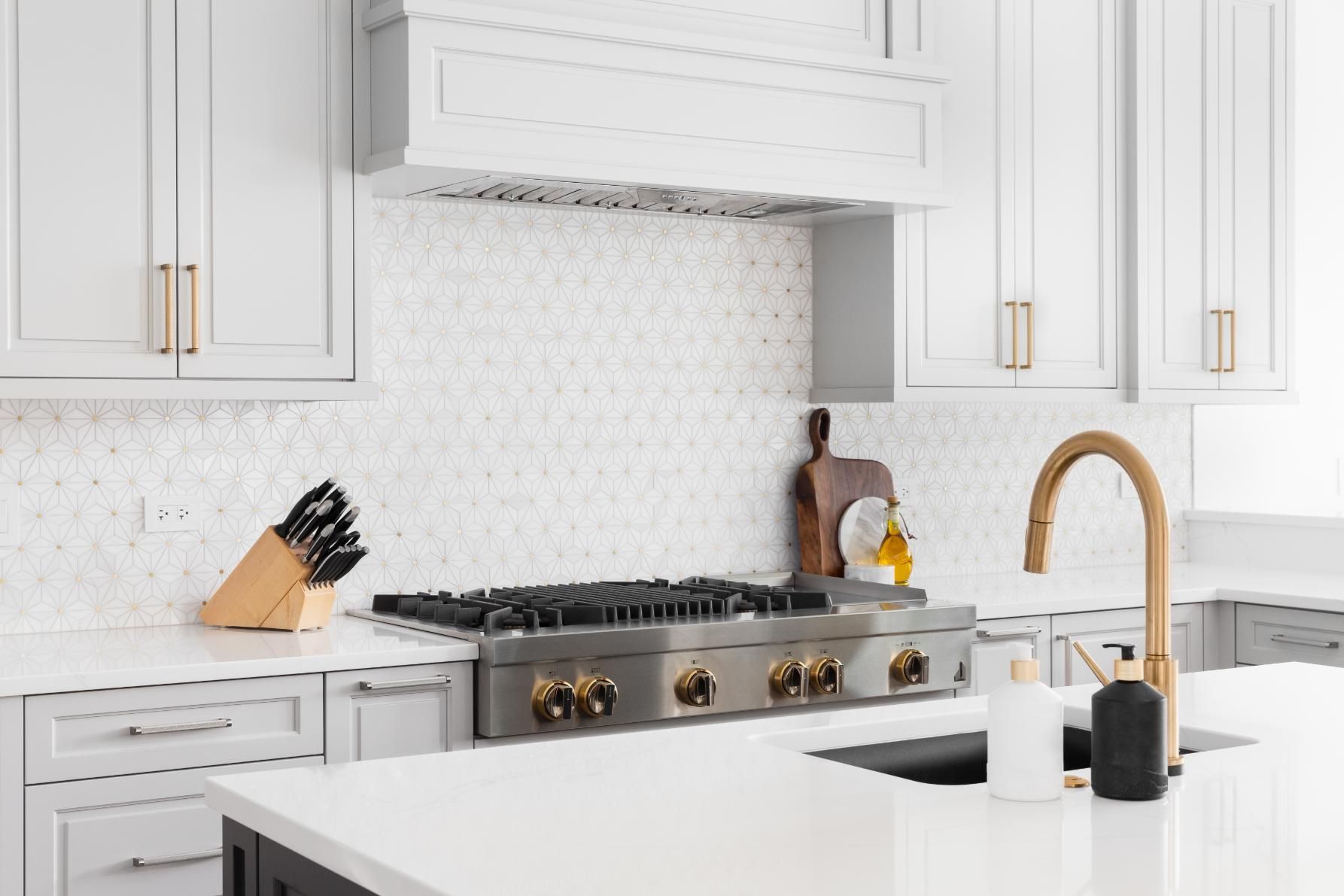Modern kitchen with white cabinets, stainless steel range, and gold fixtures.