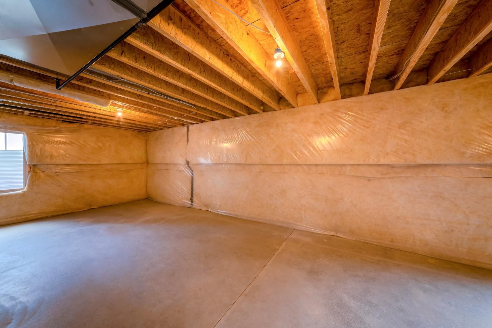 Empty unfinished basement with concrete floor, exposed wooden ceiling, and insulated walls.