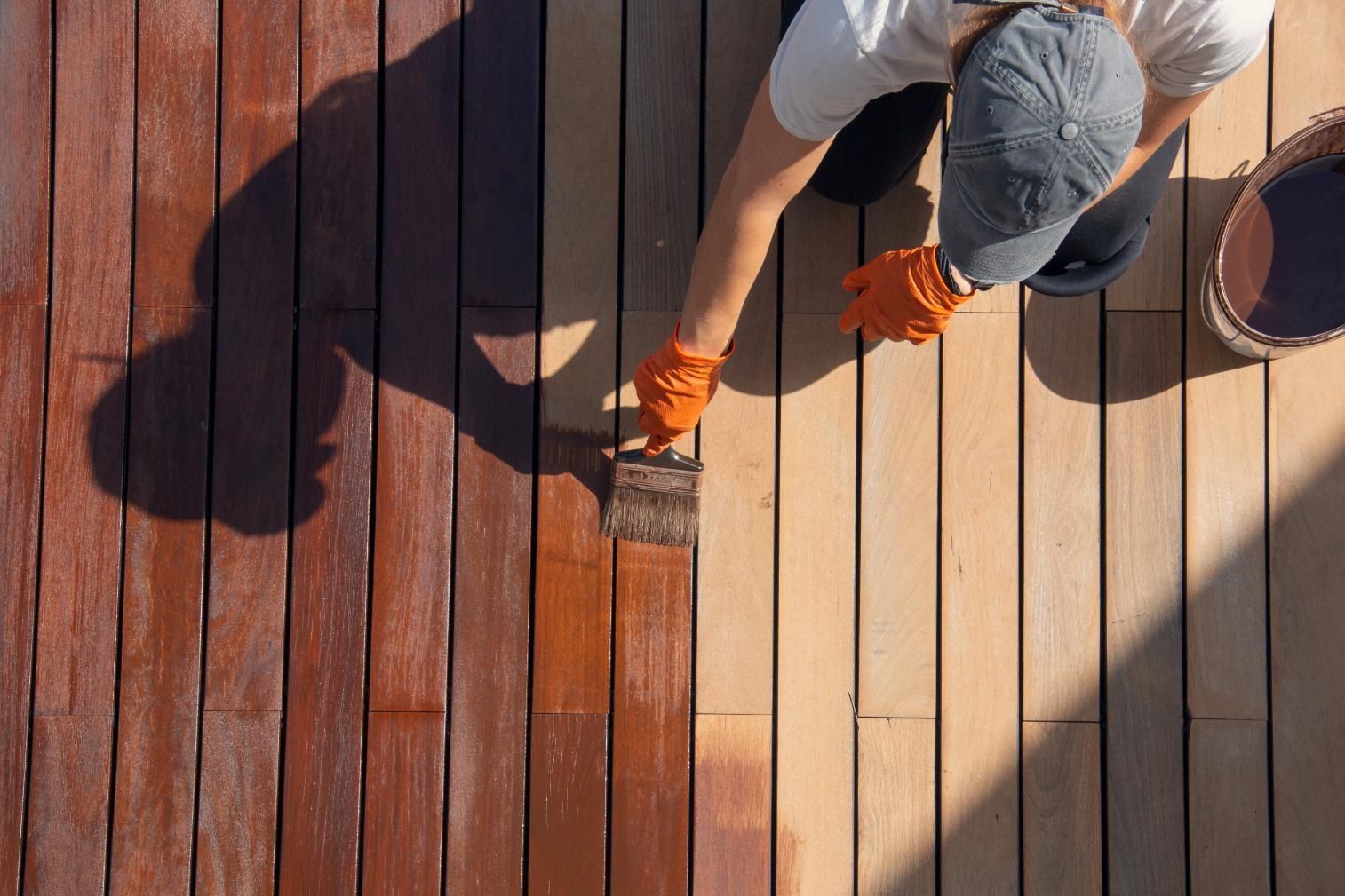 Person applying stain to wooden planks with a brush; bucket nearby.