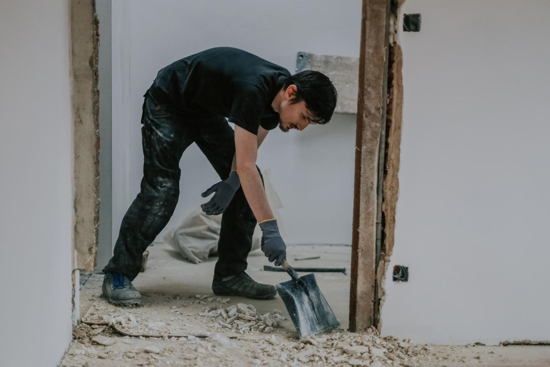 Person in black clothing using a shovel to clean debris in a doorway.