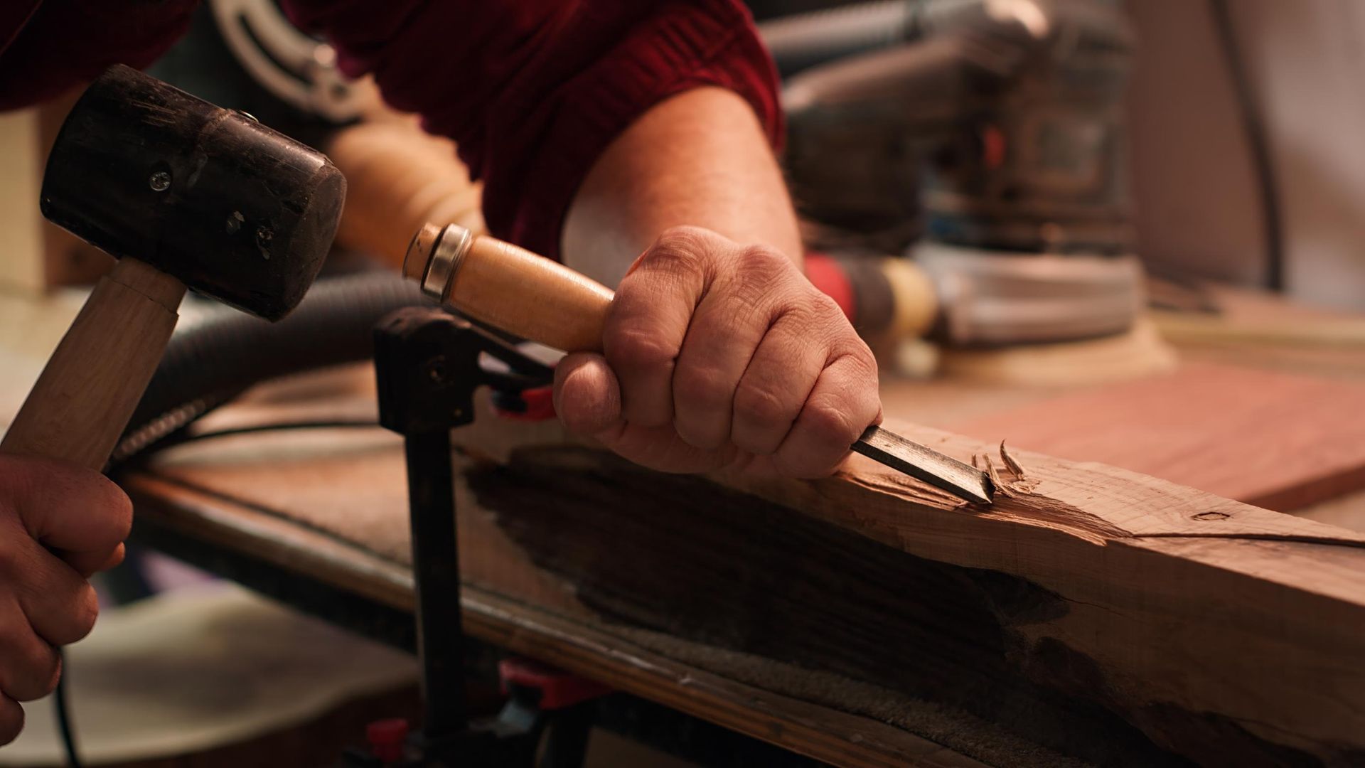 Person using a mallet to chisel wood clamped to a workbench.