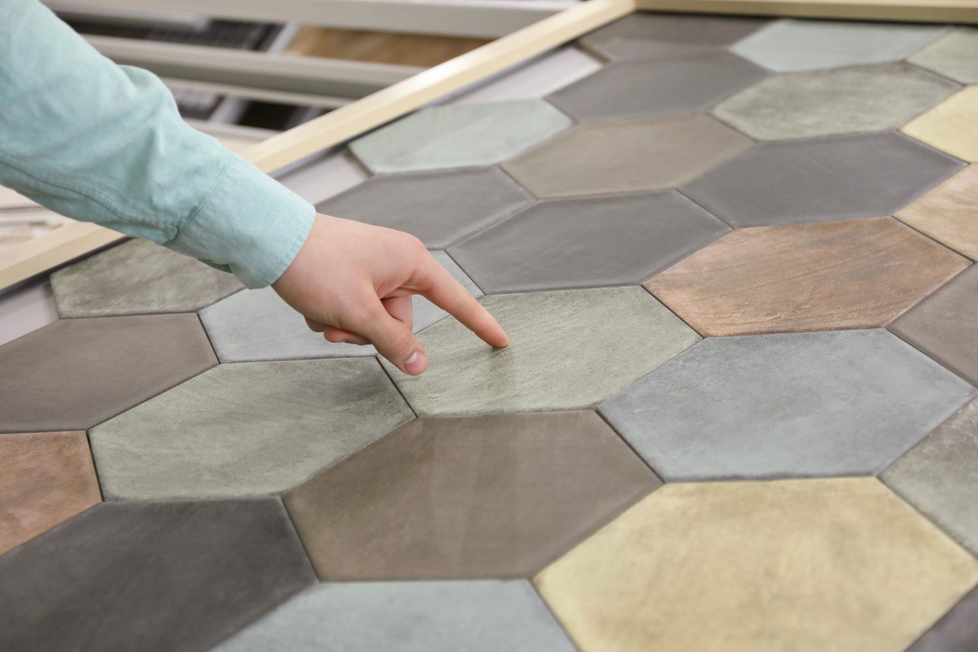 Hand pointing at a light brown hexagonal tile in a display of various colored tiles.