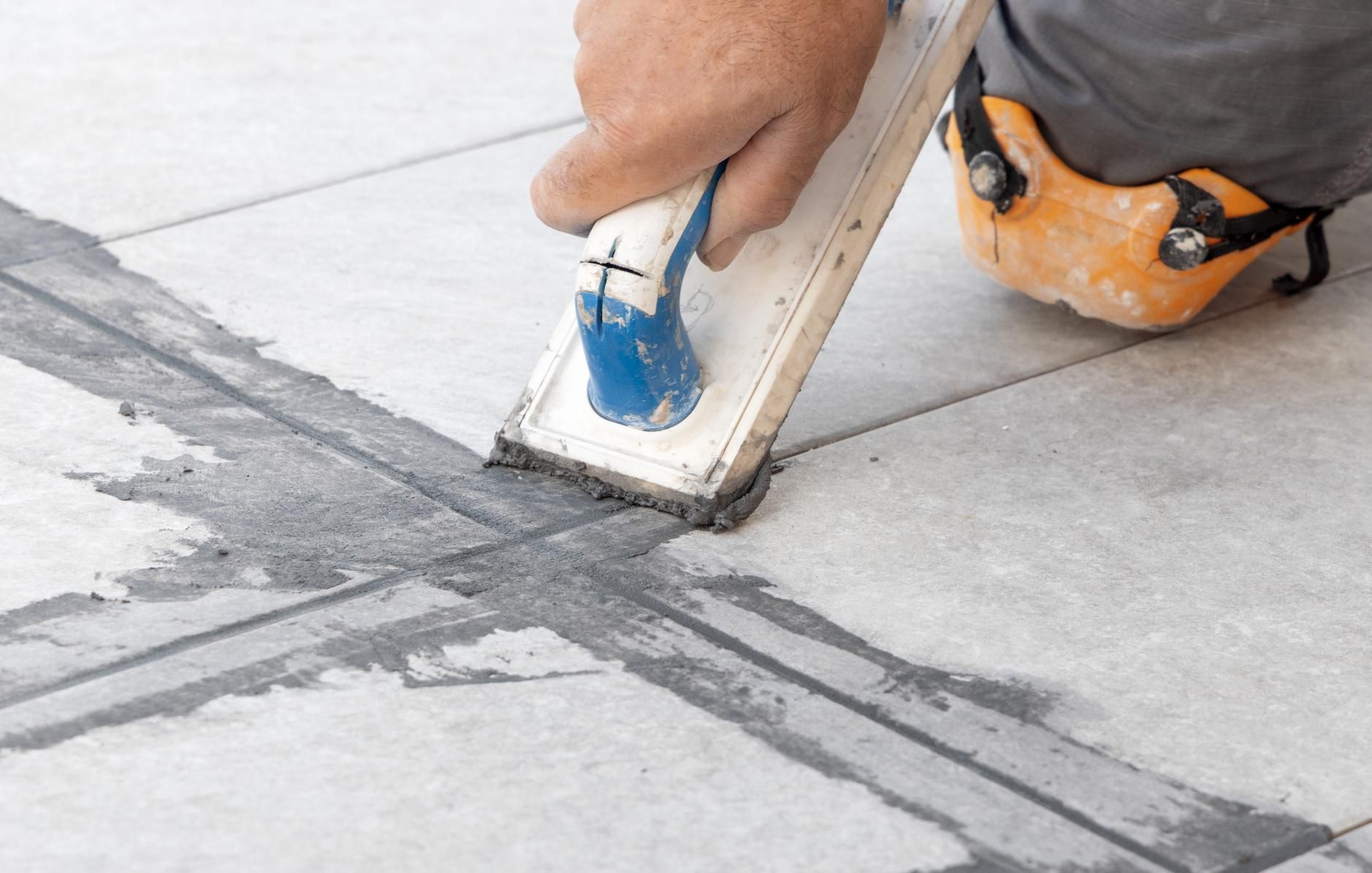 Person using a trowel to apply grout to floor tile joints.