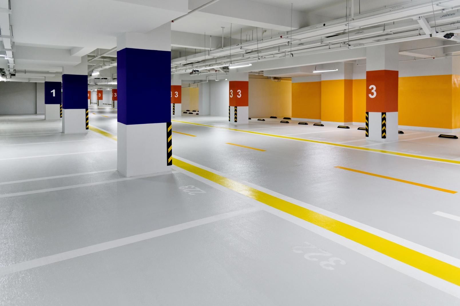 Empty, modern parking garage with blue, orange and white pillars and yellow lane markings.