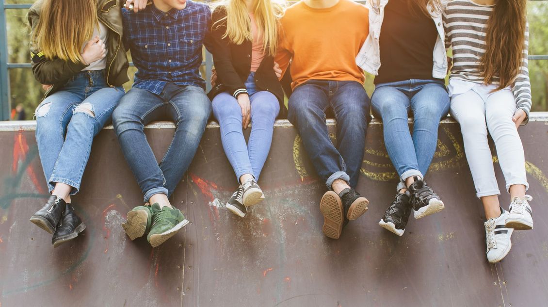 A group of young people are sitting on a wall with their legs crossed.