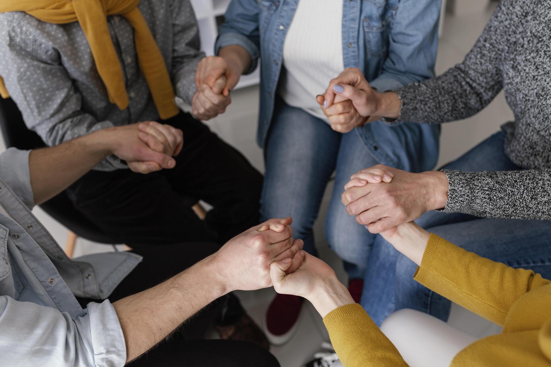 A group of people are sitting in a circle holding hands.