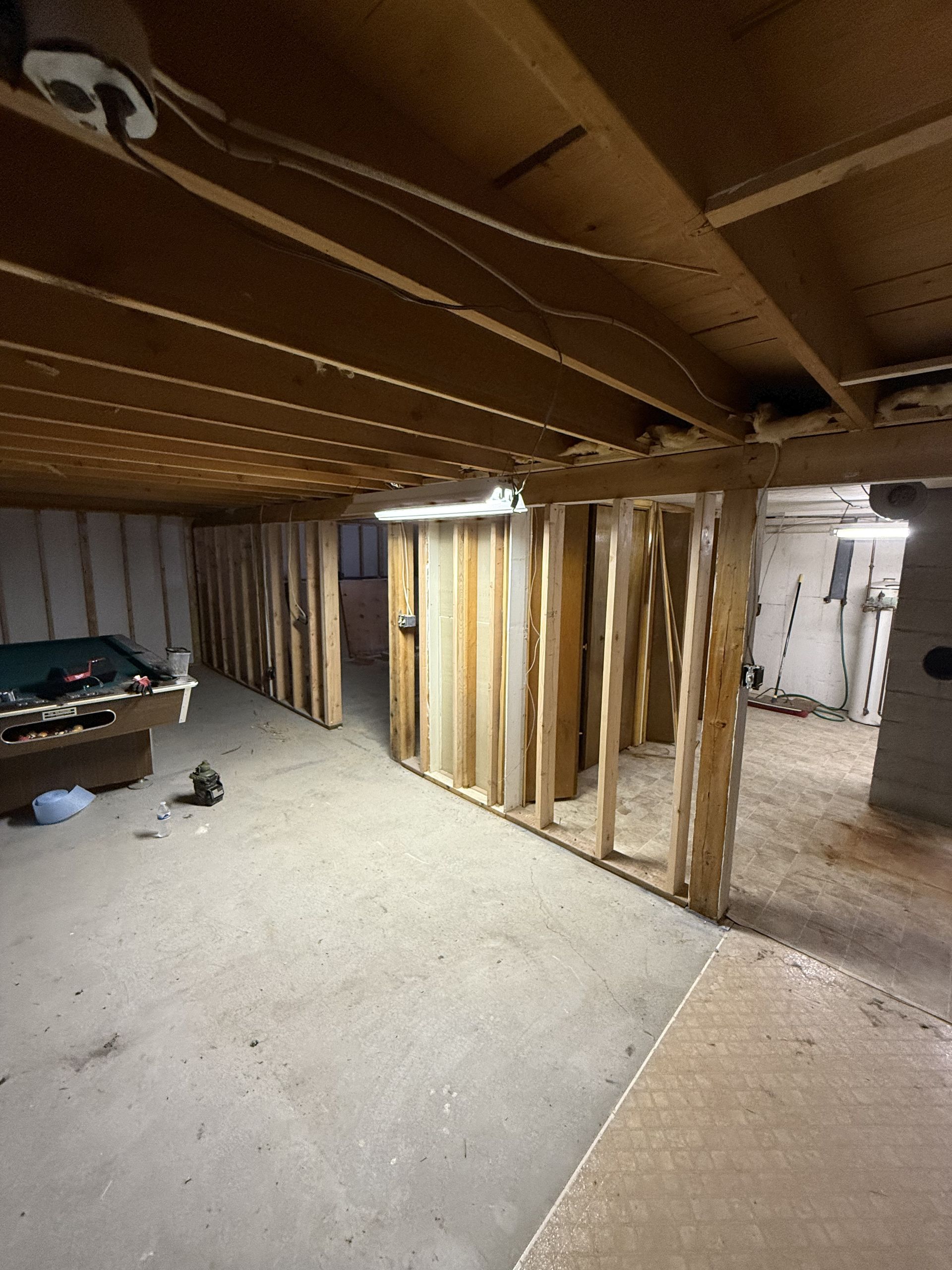 Basement under construction with exposed wooden framing. Concrete floor, exposed ceiling beams, and unfinished walls.