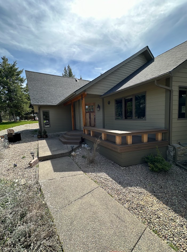 A light green house with a walkway leading to the entrance. The entrance has wooden supports, and the walkway has gray concrete.